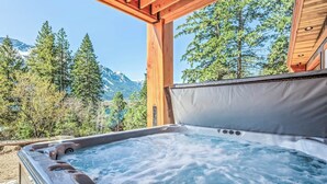 A hot tub with a control panel, surrounded by wooden beams and a view of trees and mountains. - Luxurious cabin on LK Wenatchee w/access & hot tub (Chelan County)