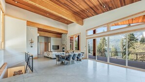 A spacious living area with a dining table and chairs, a fireplace, and large windows offering a view of the outdoors. - Luxurious cabin on LK Wenatchee w/access & hot tub (Chelan County)