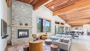 A spacious living area with a stone fireplace, large windows, and a modern kitchen. - Luxurious cabin on LK Wenatchee w/access & hot tub (Chelan County)
