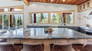 A modern kitchen with a large island, wooden ceiling, and large windows offering a view of trees. - Luxurious cabin on LK Wenatchee w/access & hot tub (Chelan County)