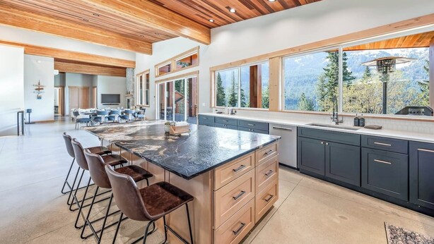 A modern kitchen with a large island, dark cabinets, and a view of mountains through large windows. - Luxurious cabin on LK Wenatchee w/access & hot tub (Chelan County)