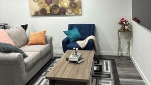 Een moderne woonkamer met een grijze bank, een blauwe fauteuil, een houten salontafel en een kamerkleed met een patroon.
