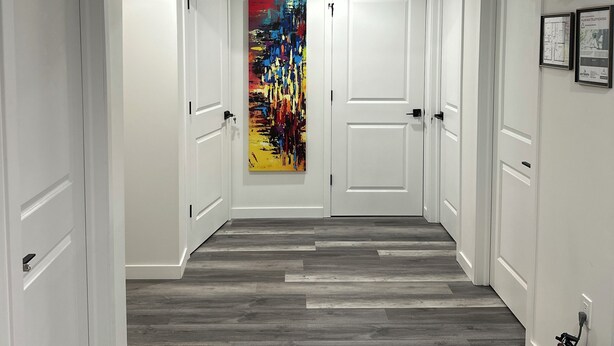 Een gang met witte deuren, een kleurrijk abstract schilderij aan de muur, een zwarte klok en een brandblusser aan de rechterkant.