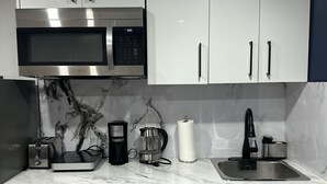 Een moderne keuken met witte kasten, een roestvrijstalen magnetron, een koffiezetapparaat en een broodrooster.