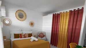 A bedroom with a bed, a nightstand, a chair, and a potted plant.