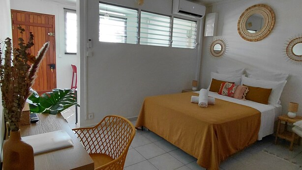 A bedroom with a bed, a desk, a chair, and a potted plant.