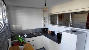 A compact kitchen with white cabinets, a black countertop, a small dining table with chairs, a potted plant, and a refrigerator.