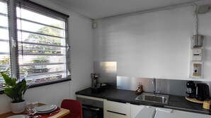 A modern kitchen with a dining area, featuring a black countertop, stainless steel appliances, and a red chair.