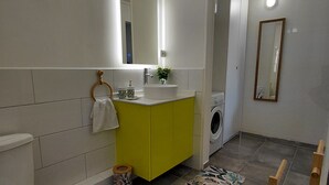 A modern bathroom with a toilet, sink, mirror, and washing machine.