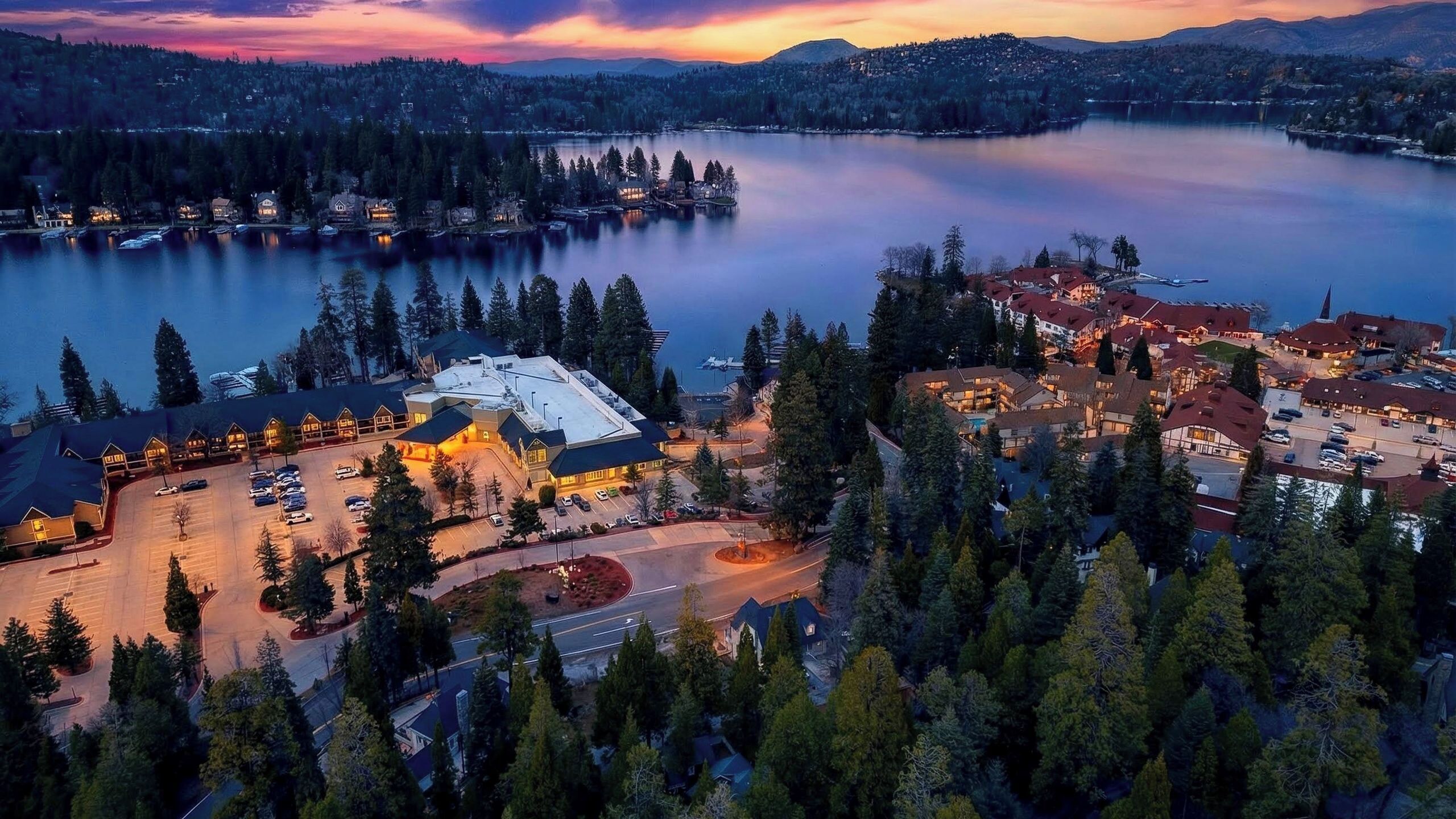 Un hotel sul lago con un parcheggio, edifici con tetti rossi e vista sul lago e sulla foresta circostante.