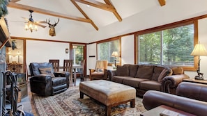 A spacious living room with leather furniture, a ceiling fan, and large windows.