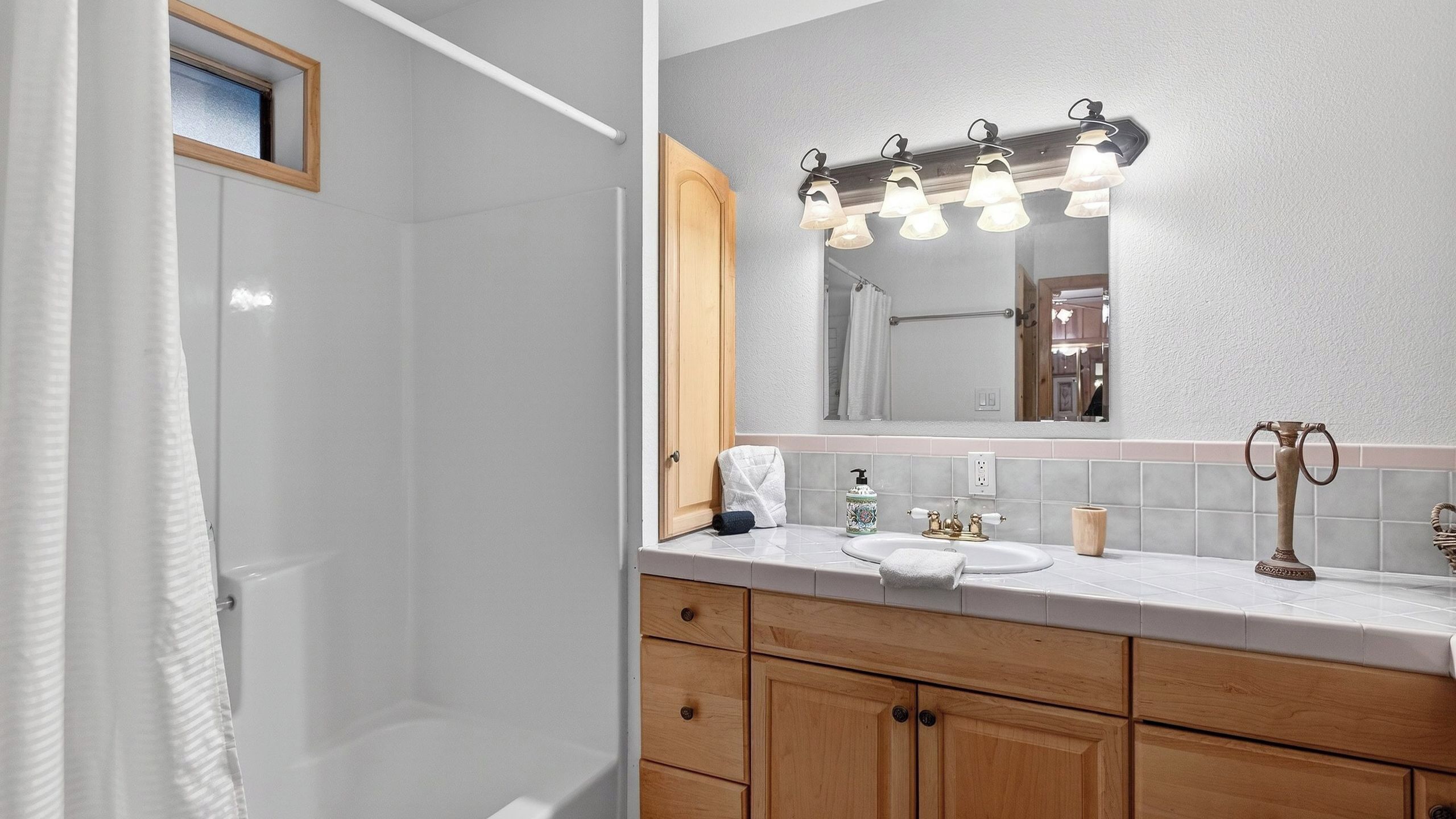 Une salle de bain avec un meuble-lavabo en bois, un évier, un miroir avec éclairage intégré et un espace douche.
