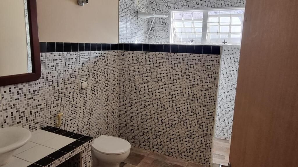Un bany amb paret de rajoles de mosaic, un vàter i un lavabo.