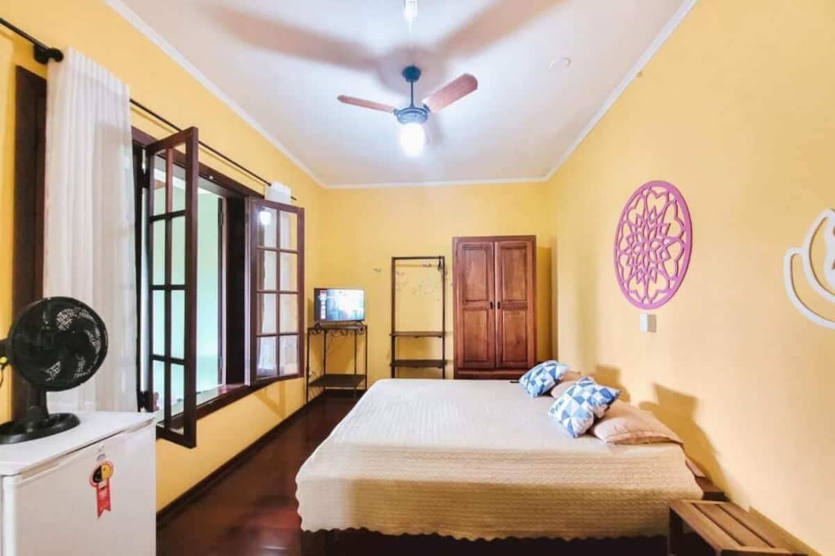 Une chambre avec un lit, un ventilateur de plafond, une petite table avec un téléviseur et une armoire.