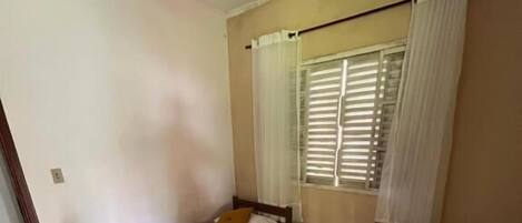 Une chambre avec deux lits simples, un ventilateur de plafond, une fenêtre avec des stores et un sol carrelé.