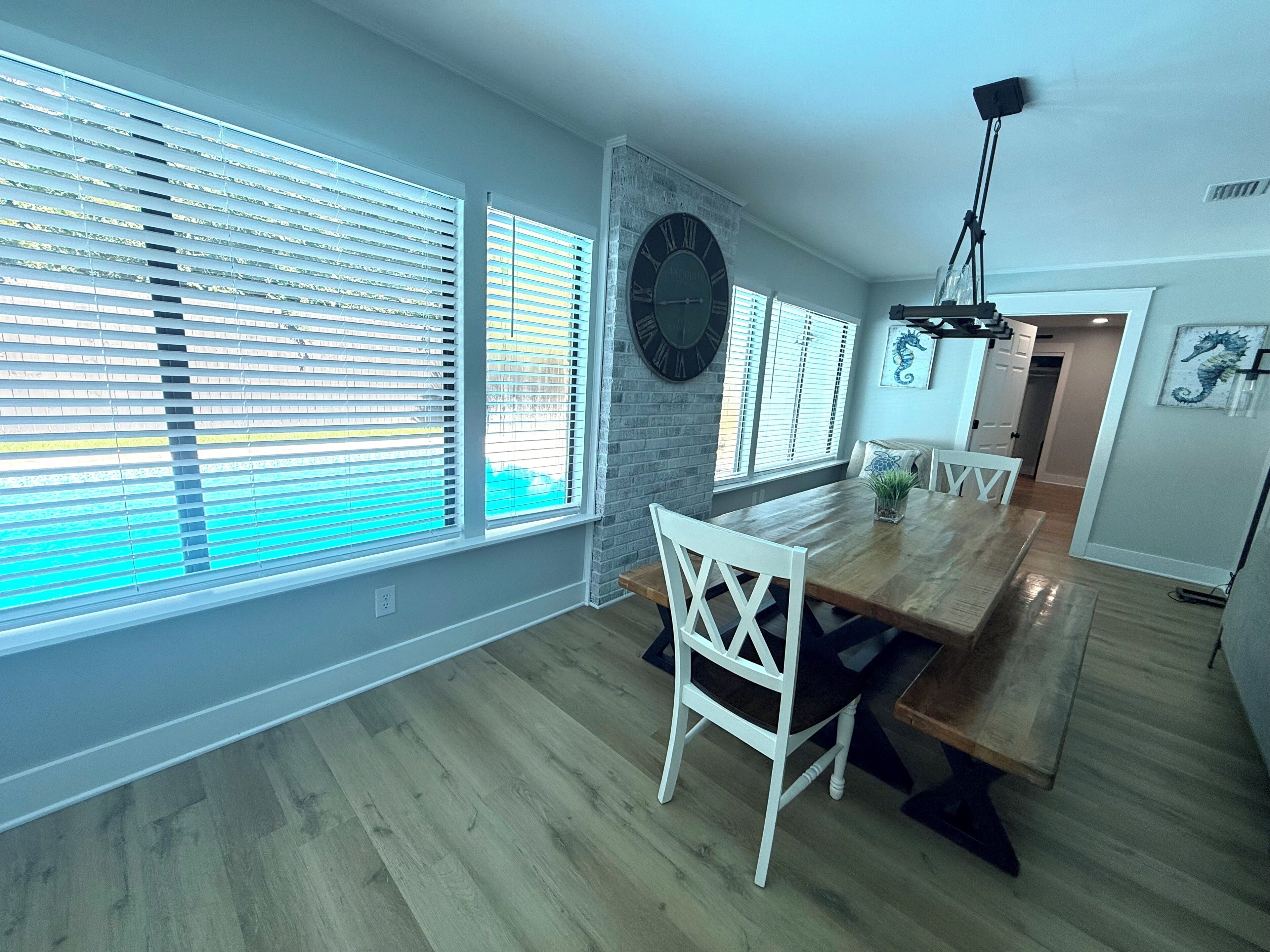 Un comedor con una mesa de madera, sillas blancas y un reloj de pared grande.