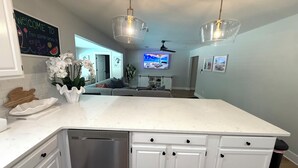 A modern kitchen with white cabinets, a dishwasher, and a large island. There is a ceiling fan and a TV mounted on the wall. - CASABELLA,4bed/2bath, 8 min from beach/ w/ POOL (Fort Walton Beach)