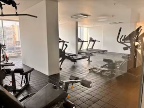 Un gimnasio con cintas de correr, máquinas de pesas y un amplio ventanal con vistas a la ciudad.
