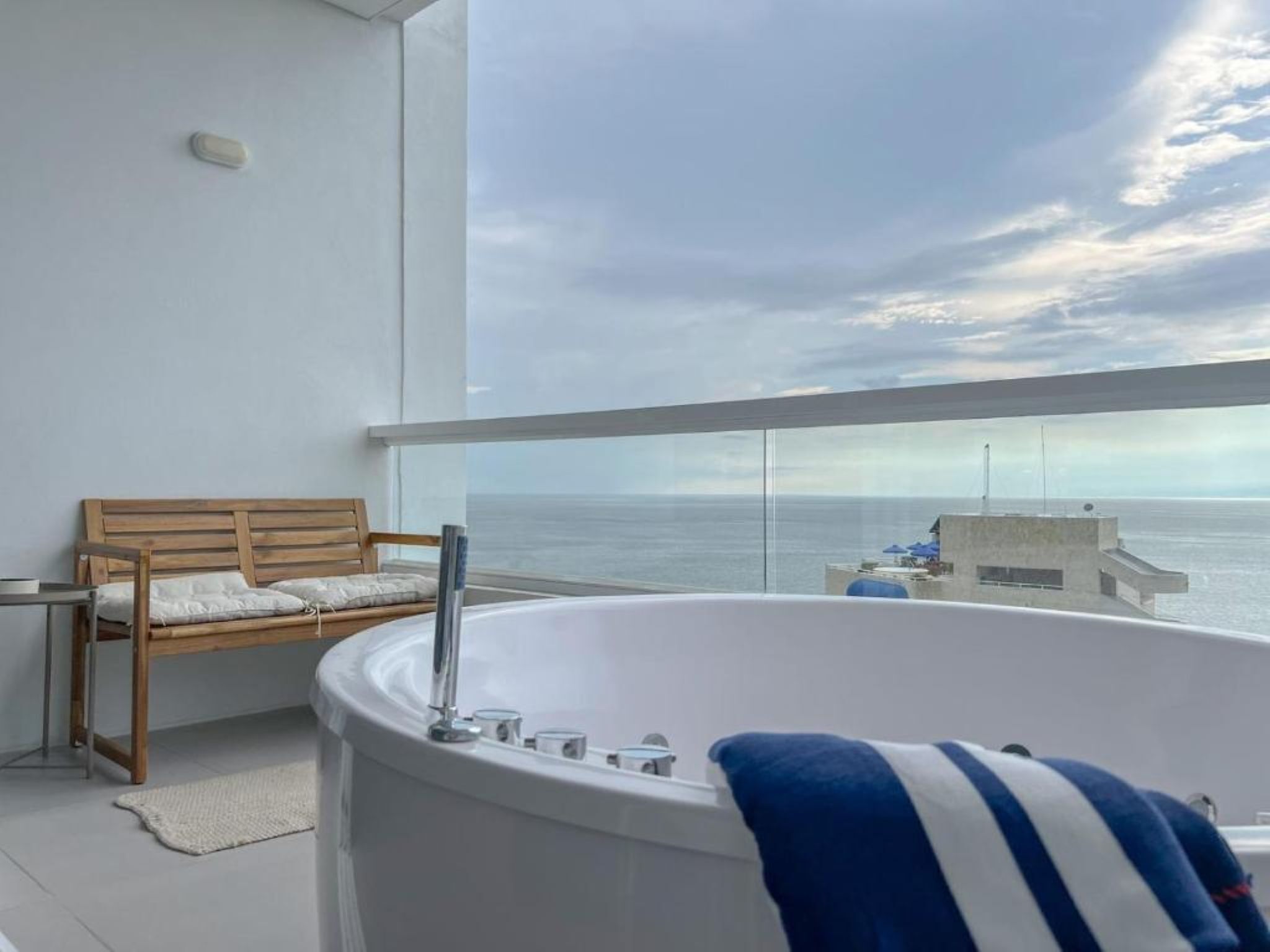 Ein Balkon mit einem Holzstuhl, einer weißen Badewanne und Blick aufs Meer.