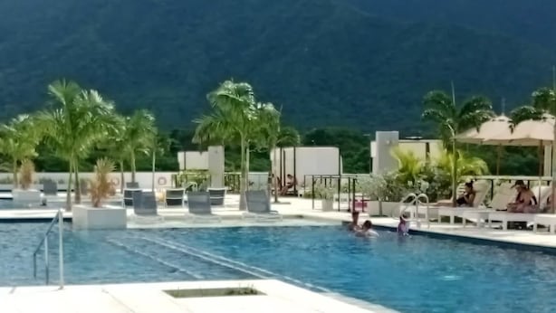 A pool area with lounge chairs and umbrellas, surrounded by palm trees and mountains in the background. - Porto Horizonte Suite 1309-Suite in Hotel in Santa Marta (Santa Marta)