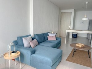 Un salon moderne avec un canapé d’angle bleu, une petite table d’appoint en bois et une table basse ronde.