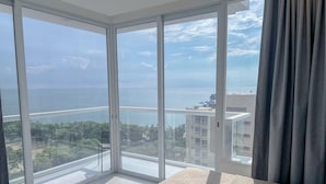 A bedroom with a large sliding glass door leading to a balcony with a view of the sea and surrounding buildings. - Porto Horizonte Suite 1309-Suite in Hotel in Santa Marta (Santa Marta)