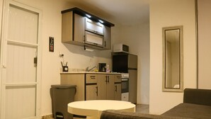 A compact kitchen with a microwave, stove, and cabinets. There's a round table and a chair in the foreground. - Mami's LITTLE Corner - Near Airport, Beaches and Malls (San Juan)