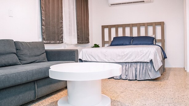 A modern bedroom with a grey sofa, a round white table, and a bed with a wooden headboard. - Mami's LITTLE Corner - Near Airport, Beaches and Malls (San Juan)