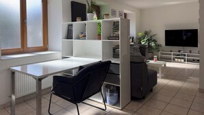 Un salon moderne avec un bureau blanc, une chaise noire, un canapé gris et un téléviseur fixé au mur.
