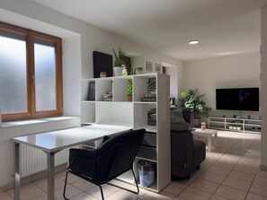 A modern living room with a white desk, black chair, grey sofa, and a TV mounted on the wall. - Escapade Coubonnaise (Coubon)