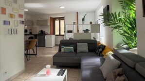 Un salon moderne avec un canapé gris, une table basse et une cuisine en arrière-plan.