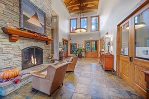 Un vestíbulo amplio con chimenea de piedra, asientos de cuero y un gran ventanal con vista al interior.