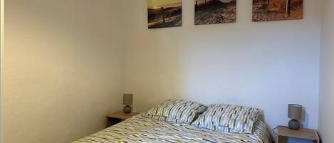 A bedroom with a bed, two bedside tables, and three wall-mounted pictures.