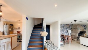 Une cuisine moderne dotée d’un four encastré, un coin repas avec une cheminée en pierre et un escalier avec une rampe bleue.
