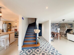 Une cuisine moderne dotée d’un four encastré, un coin repas avec une cheminée en pierre et un escalier avec une rampe bleue.