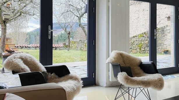 Un salon moderne avec deux fauteuils confortables, une table basse et une vue sur un jardin grâce à de grandes portes vitrées.