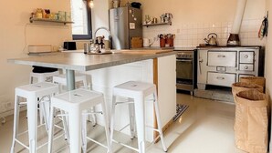 Une cuisine dotée d’un îlot central, de tabourets de bar blancs, d’un réfrigérateur, d’une cuisinière et de divers ustensiles de cuisine.