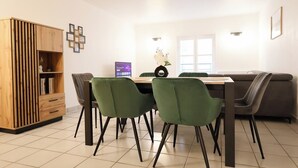 Un comedor moderno con un armario de madera, sillas verdes, una mesa de comedor y un sofá gris.