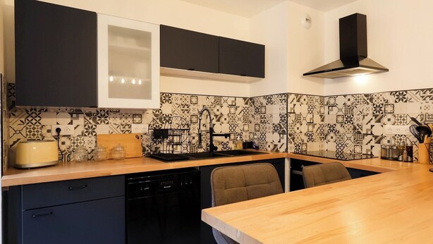 Una cocina moderna con armarios negros, encimera de madera, lavavajillas integrado y salpicadero con diseño.