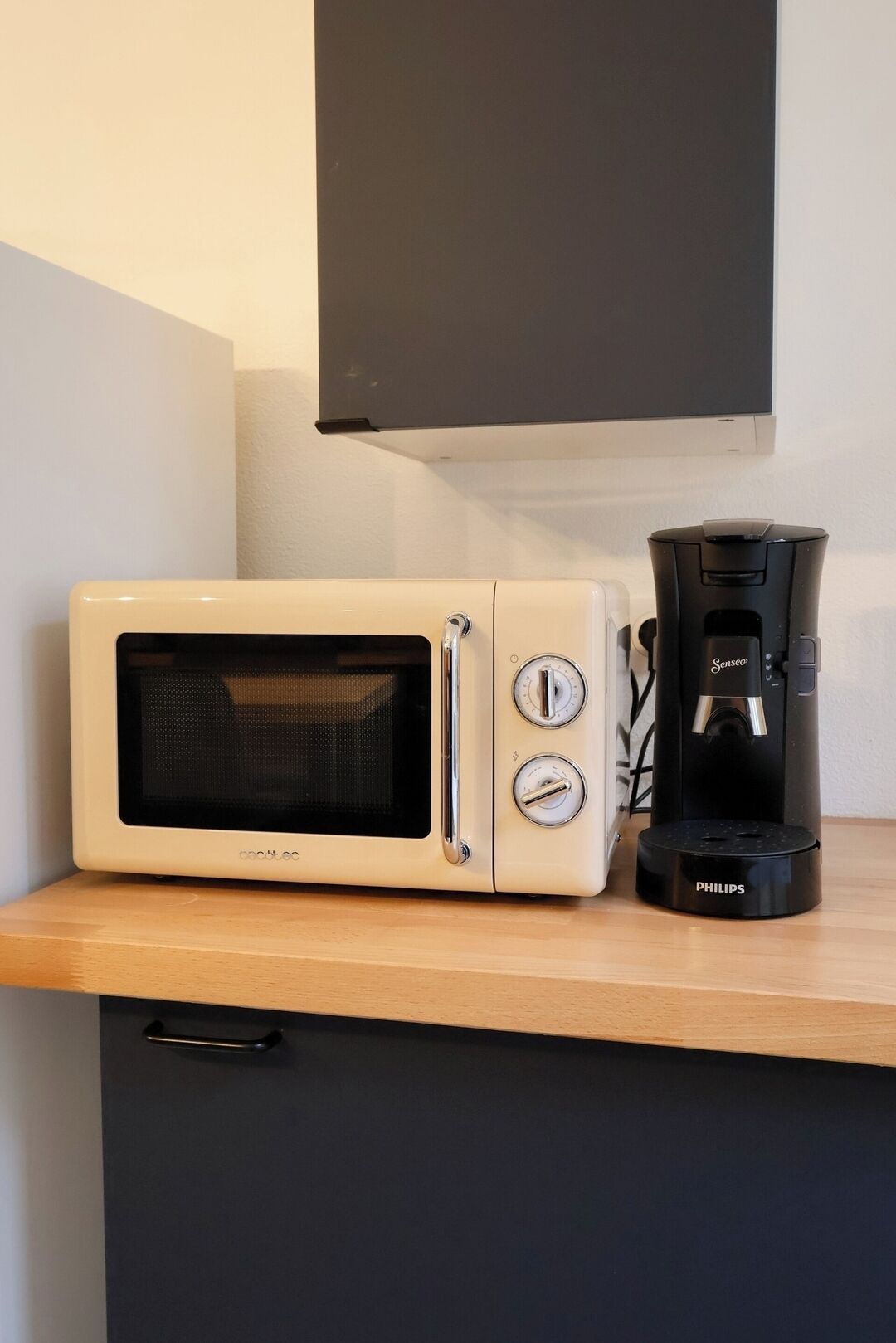 A microwave and coffee maker on a wooden countertop with a black cabinet below.