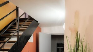 Una escalera con barandilla metálica, una puerta y un suelo con diseño. Hay dos plantas en macetas sobre una superficie blanca.