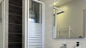 Une salle de bain moderne avec une douche à parois de verre, un meuble-lavabo avec des tiroirs, un évier et un miroir.