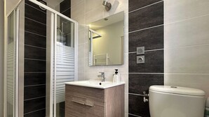 Une salle de bain moderne avec une douche à l’italienne, un meuble-lavabo avec un miroir et des toilettes.