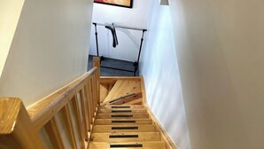 Een houten trap met een leuning, leidend naar een plateau met een plafondlamp en een lijstwerkfoto.