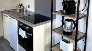Een kleine keuken met een ingebouwde kookplaat, oven en magnetron. Op een plank staan een koffiezetapparaat, waterkoker en broodrooster.