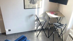 Een kamer met een blauwe bank, een kleine tafel met een stoel, een flatscreen televisie en een poster aan de muur.