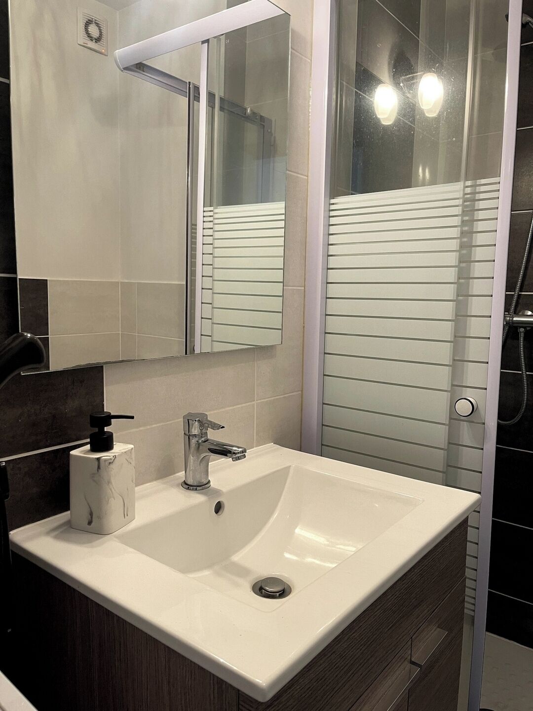 Un baño moderno con un lavamanos blanco, un espejo y un box de ducha de vidrio.