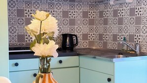 Een keuken met lichtgroene kastjes, een betegelde achterwand en een houten tafel met een strepenvaas vol witte bloemen.