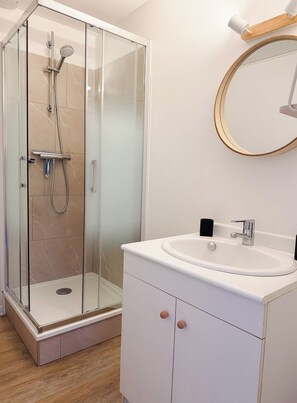 Un baño moderno con ducha de vidrio, un lavamanos blanco y un espejo redondo.