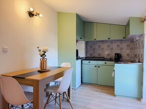 Une cuisine de taille réduite avec des meubles de couleur verte, un pare-feu décoré et une table à manger en bois, accompagnée de chaises.